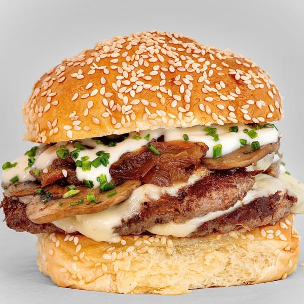 Gourmet burger with two patties, melted cheese, mushrooms, caramelized onions, and chives on a sesame bun.