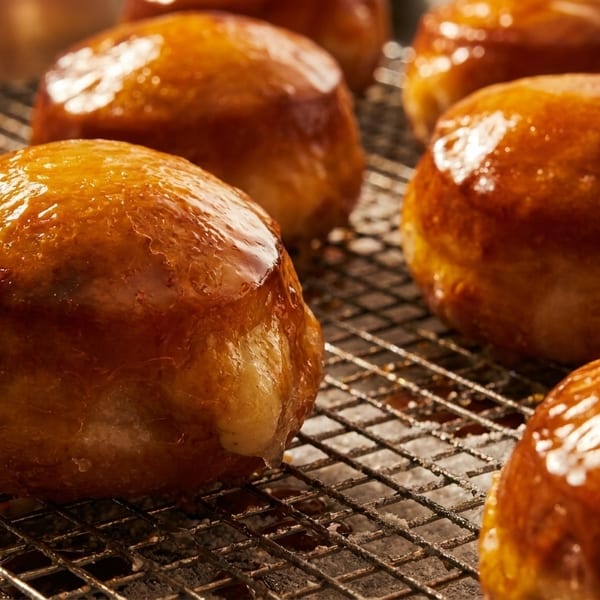 Several golden-brown, glazed pastries, possibly donuts or buns, resting on a metal cooling rack.
