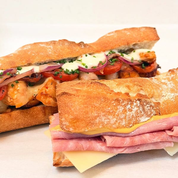 Two baguette sandwiches, one with chicken, tomatoes, and onions, the other with ham and cheese.