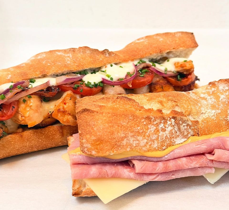 Two baguette sandwiches, one with chicken, tomatoes, and onions, the other with ham and cheese.