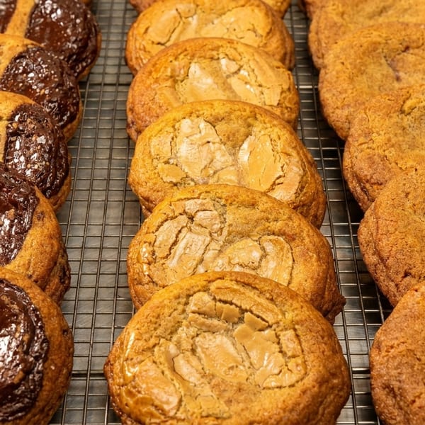 Rows of fresh-baked cookies, including chocolate chip, peanut butter, and snickerdoodle, on a cooling rack.